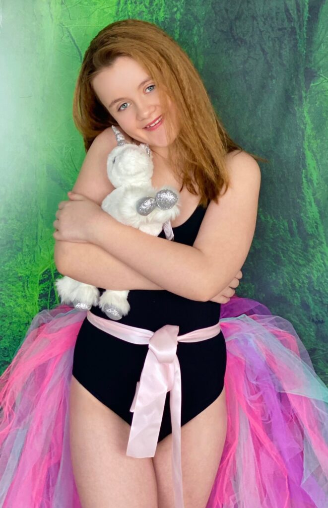 Young girl in a pastel tutu hugging a plush unicorn at a kids’ Unicorn Adoption Party.