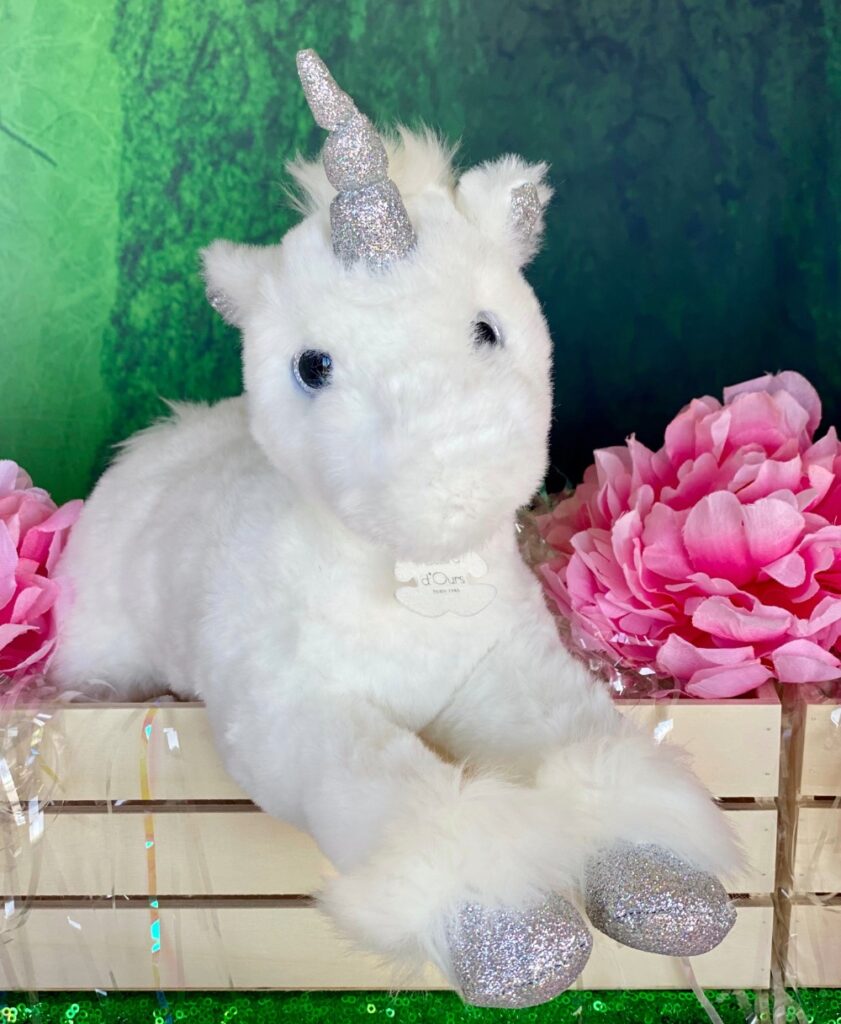 Close-up of a plush white unicorn in a wooden crate with pink flowers at a kids’ Unicorn Adoption Party.