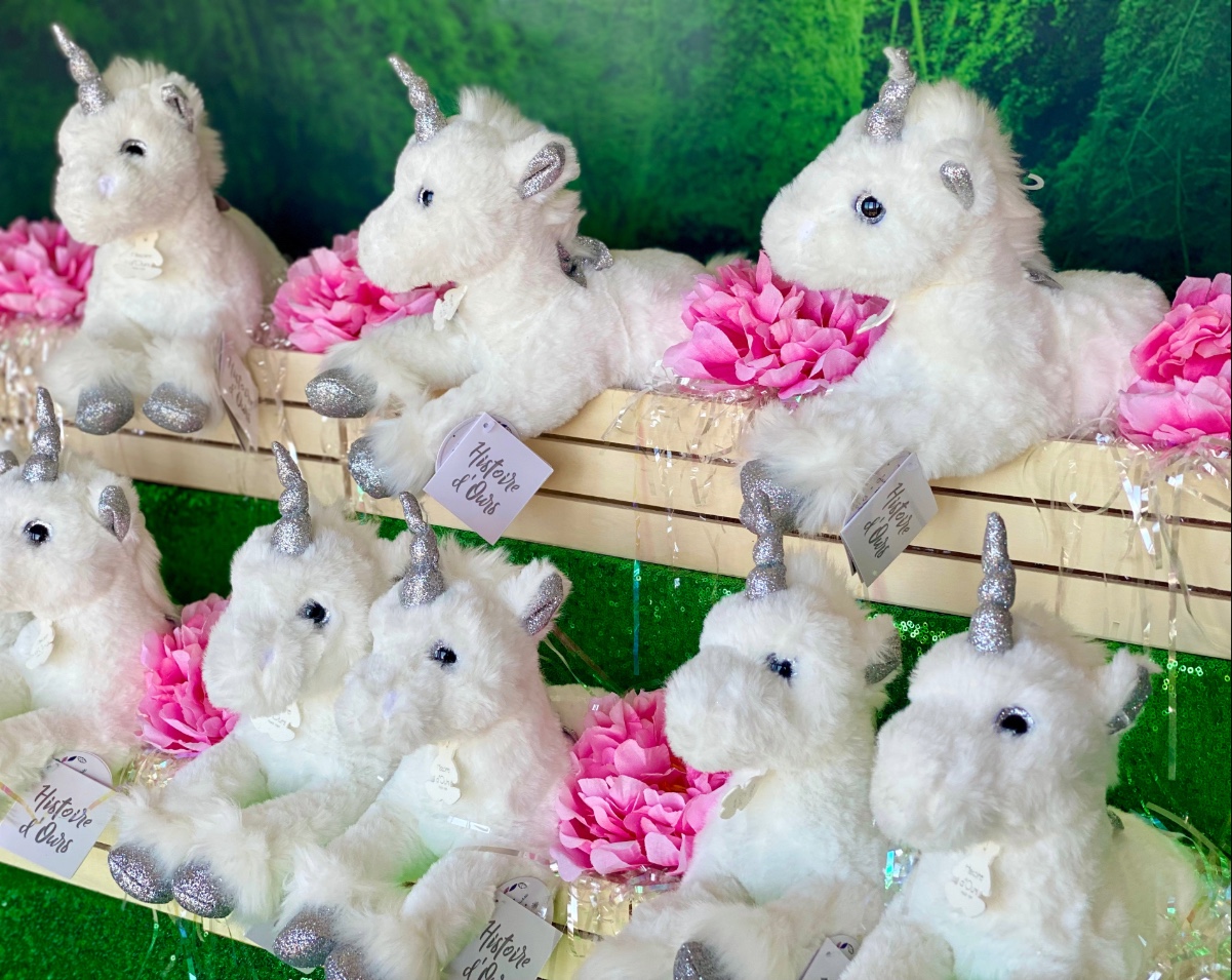 White plush unicorn party favours displayed in wooden crates with pink flowers for a kids unicorn themed party.