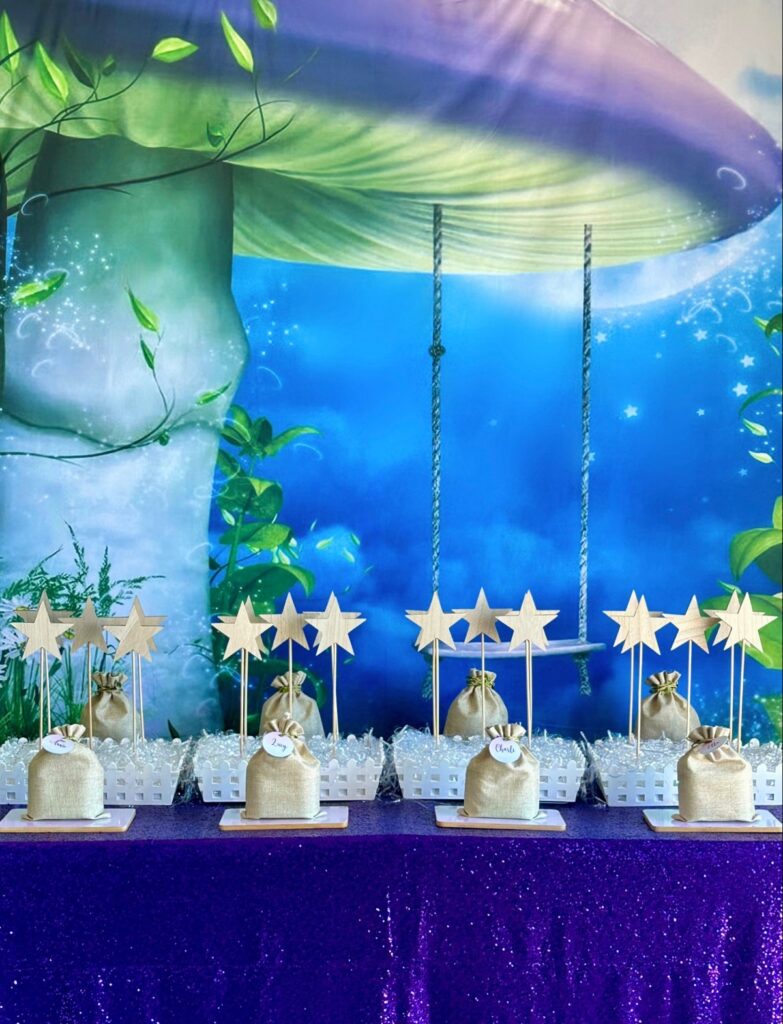 DIY fairy wand party table with purple sequin tablecloth, mushroom swing backdrop, star wands in white crate displays and hessian bags with decorating supplies.