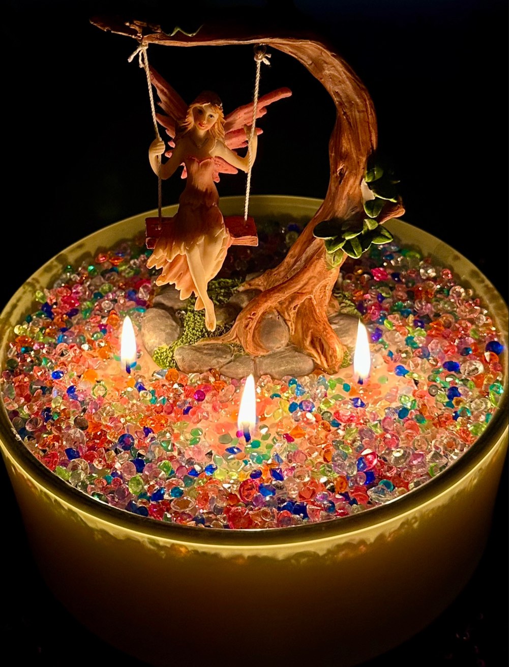 Close-up of a glowing fairy candle at a kids candle decorating party, with a fairy on a swing and crystal gems.