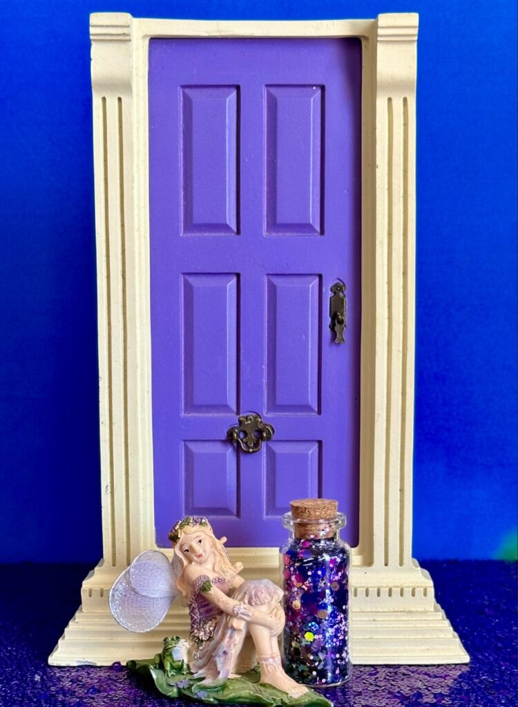 Glitter fairy potion spell jar displayed beside a miniature fairy and purple fairy door for a kids fairy party activity.
