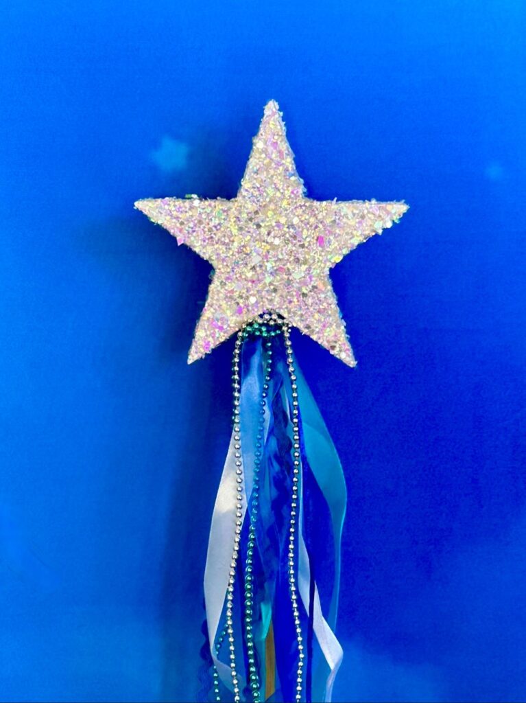 Close-up of silver glitter fairy wand with blue and silver ribbons and decorative trims hanging from the handle.