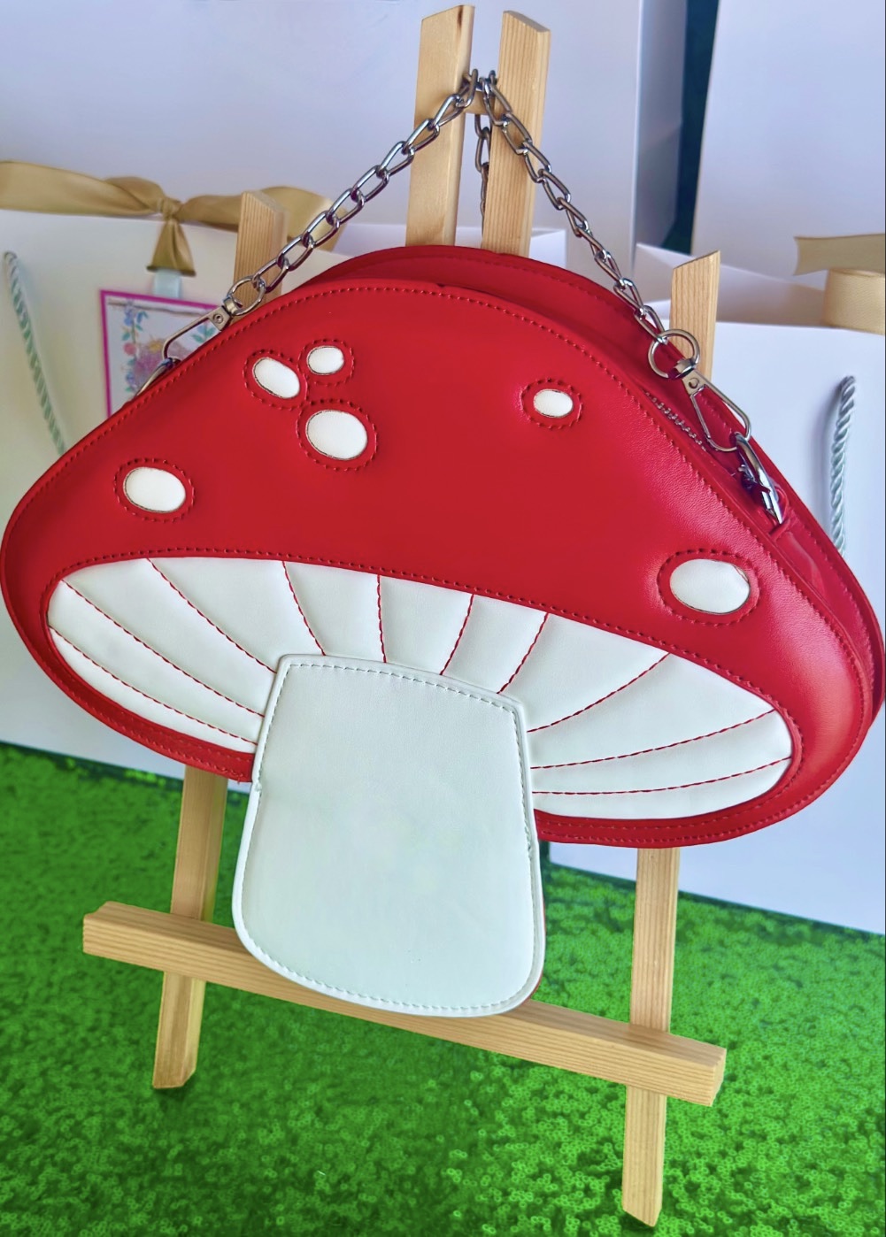 Angled view of a red and white toadstool handbag displayed on an easel at a kids fairy party favour table.