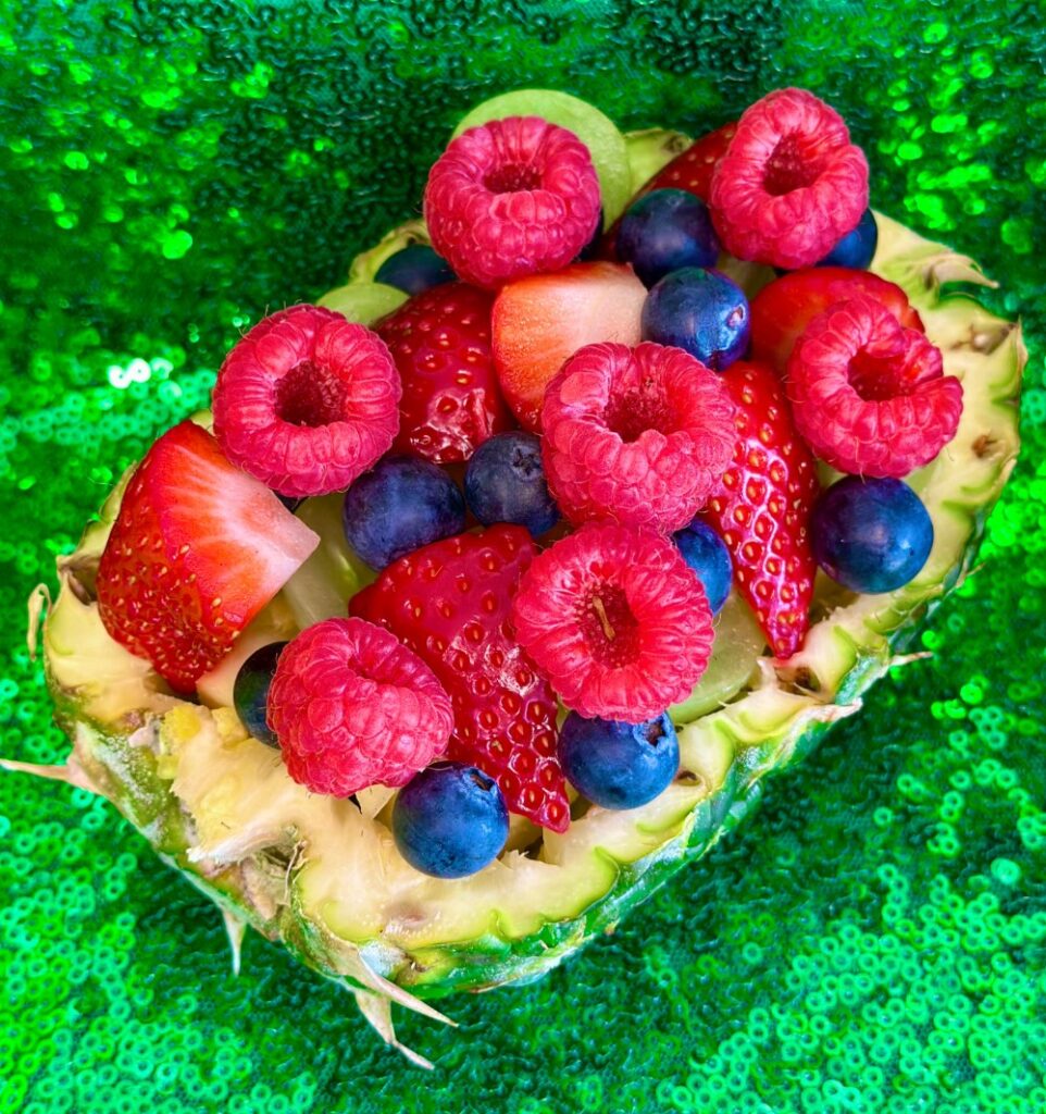 Hollowed-out pineapple half filled with berry fruit salad at a kids pineapple party food station.