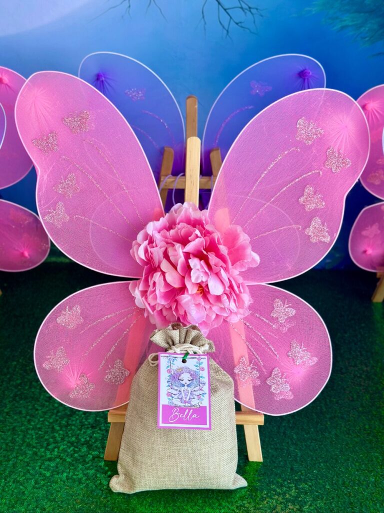 Undecorated pink fairy wings displayed on an easel with a hessian bag of decorating supplies in front for a DIY fairy wings party activity.
