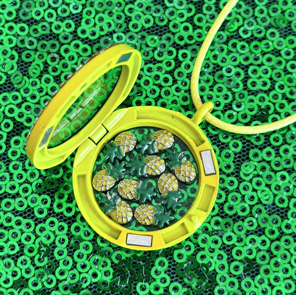 Open yellow pineapple floating locket filled with pineapple charms for a kids DIY pineapple jewelry party activity.