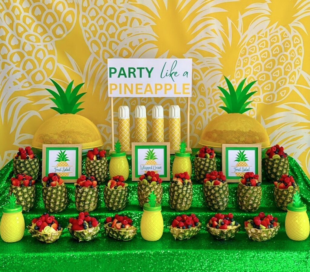 Pineapple fruit salad station for a kids party with berry fruit salad served in pineapples, a Party Like a Pineapple sign, and tropical table decorations.
