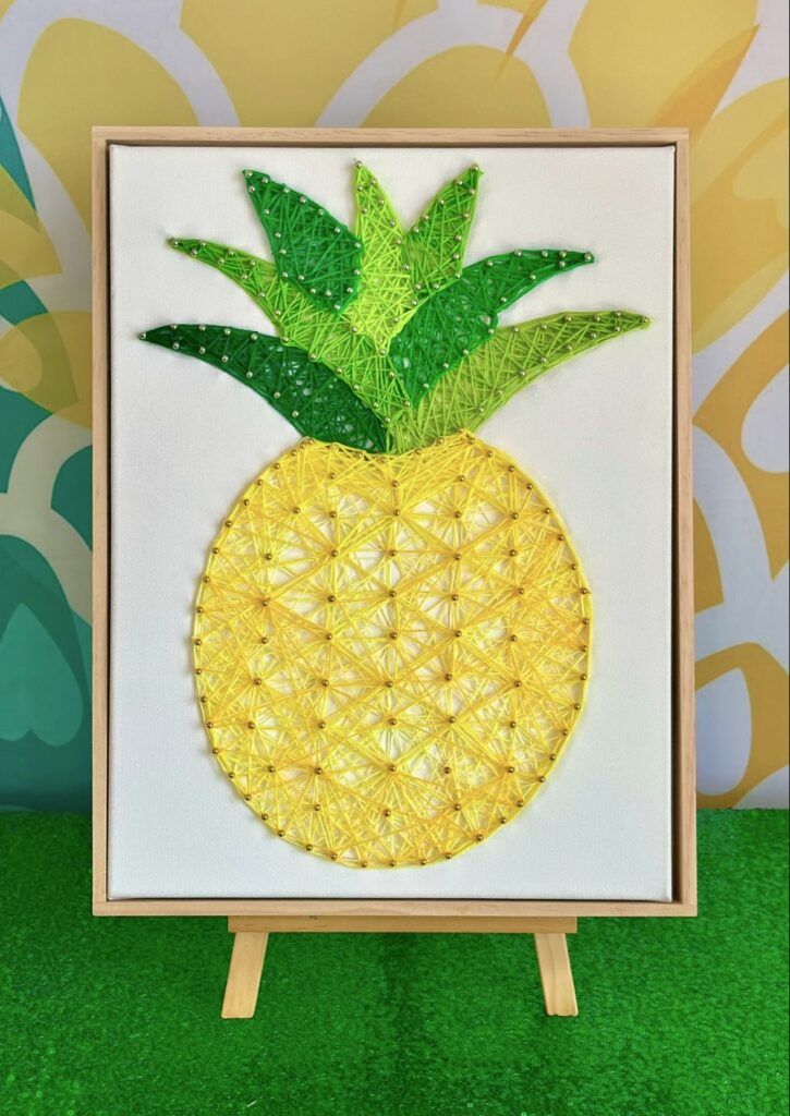 Framed pineapple string art canvas displayed on a wooden easel.