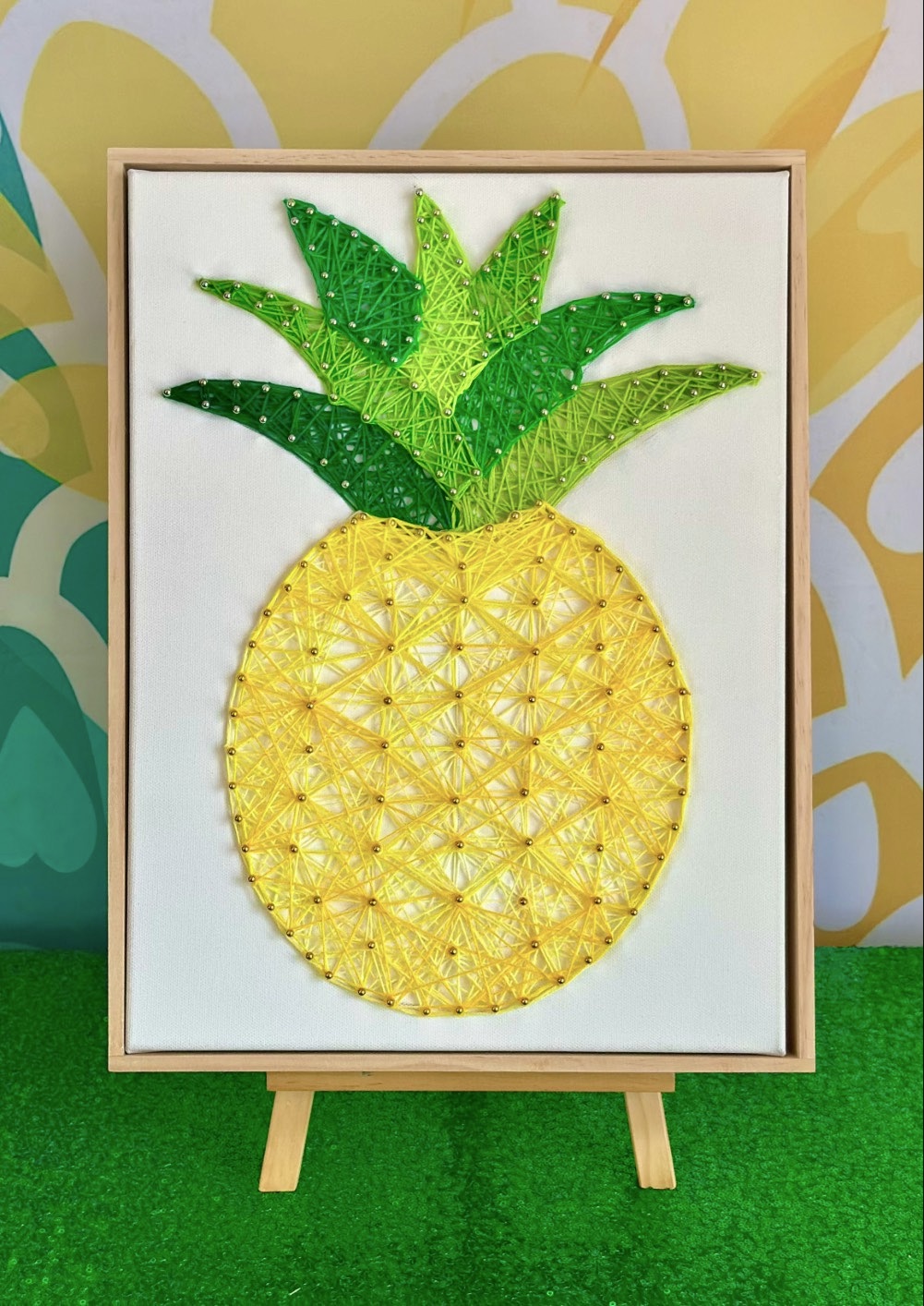 Framed pineapple string art canvas displayed on a wooden easel.