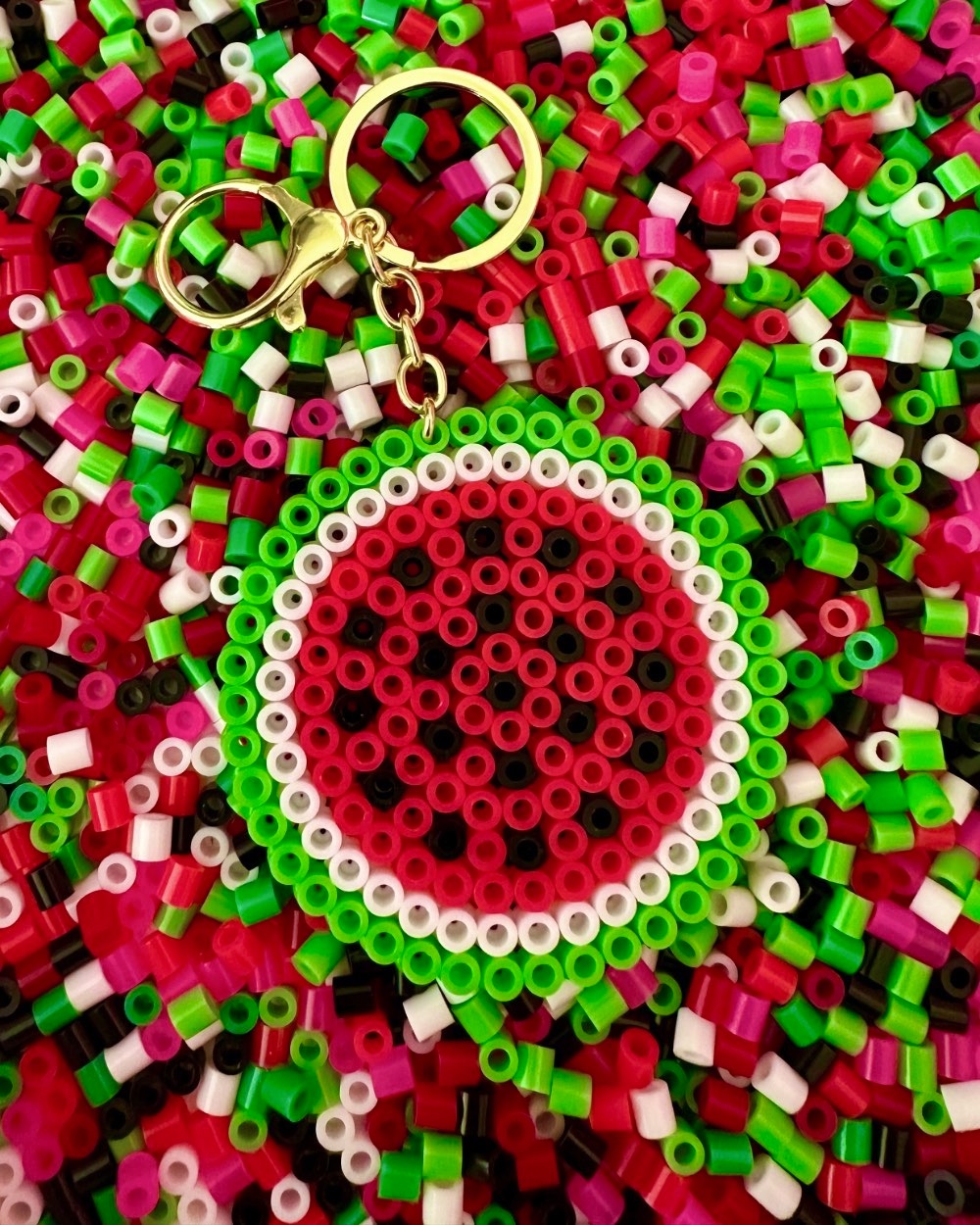 Round watermelon Perler bead keychain displayed on colourful red, green, white and black beads.